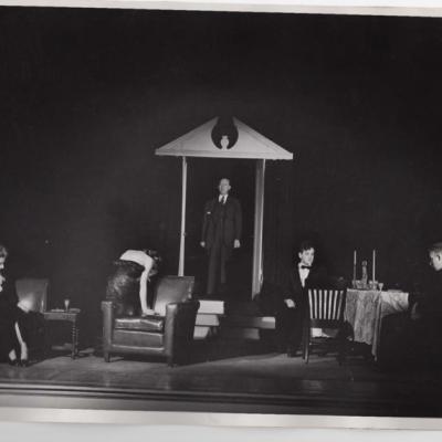 A dark black and white photograph of four actors on the set of An Inspector Calls